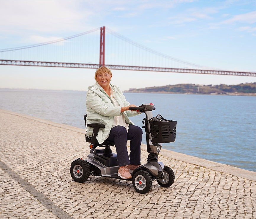 Pessoa sentada em scooter de mobilidade reduzida perto de uma ponte