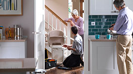 man working on stairlift with lady talking and guy making drinks